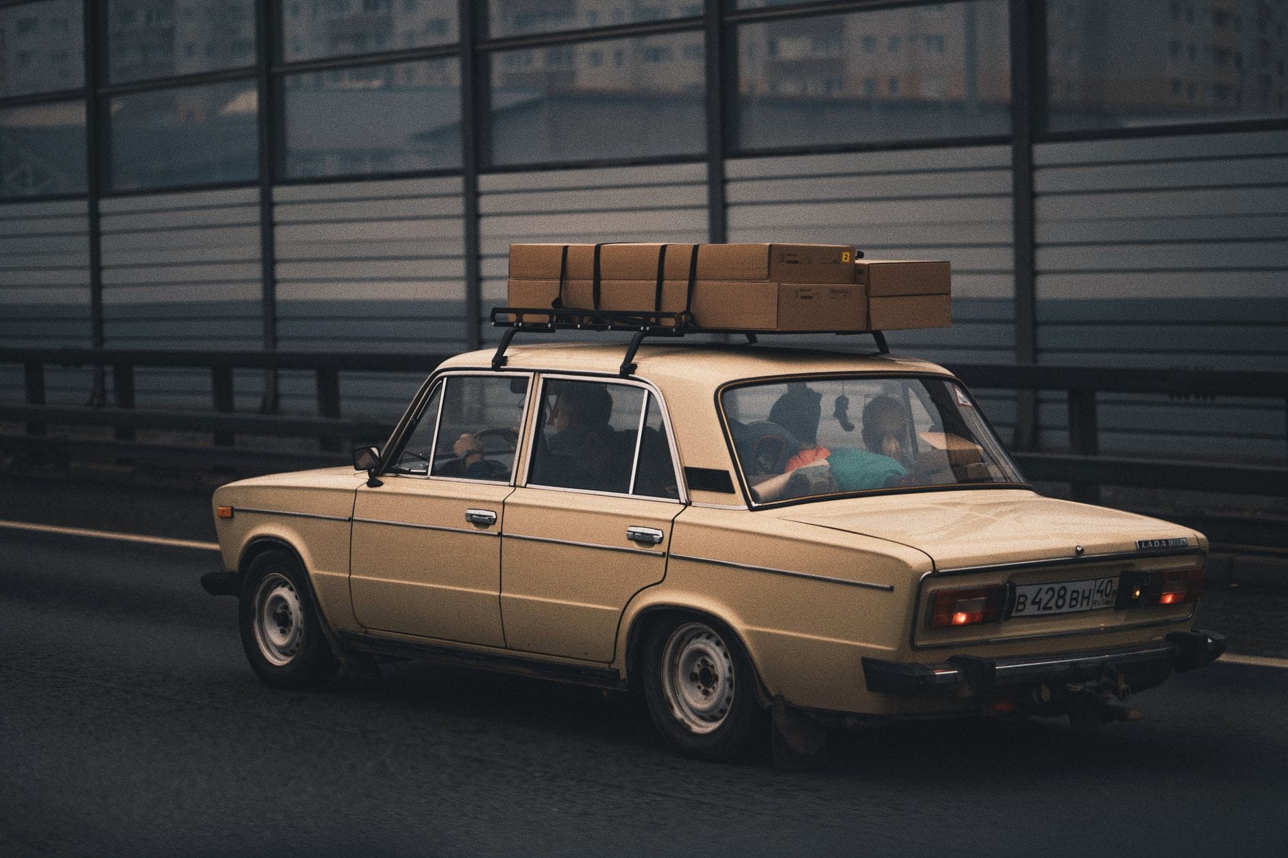 Beżowy sedan z bagażami na dachu jedzie autostradą w stronę miasta