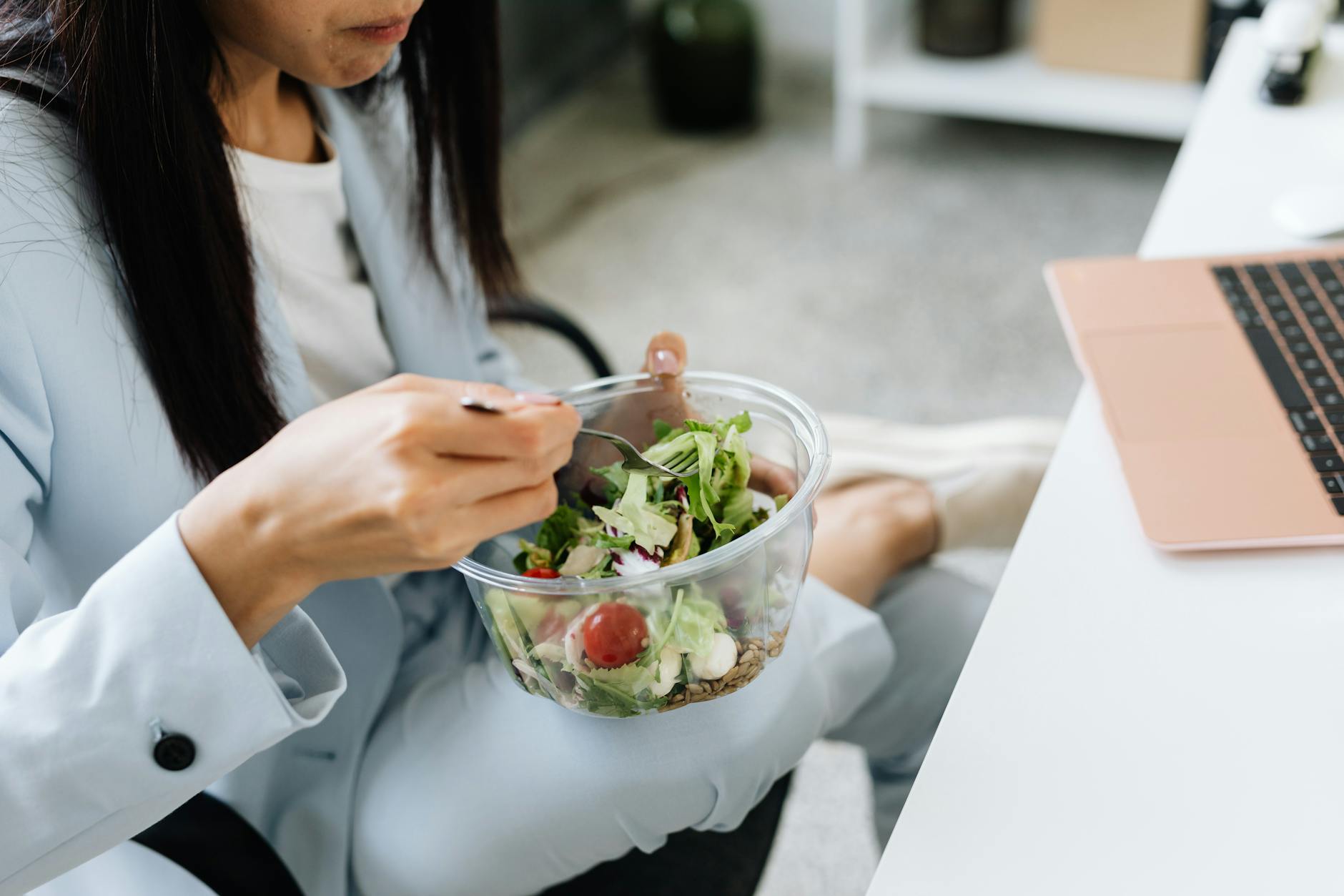 Kobieta przy biurku w pracy je sałatkę warzywną na lunch
