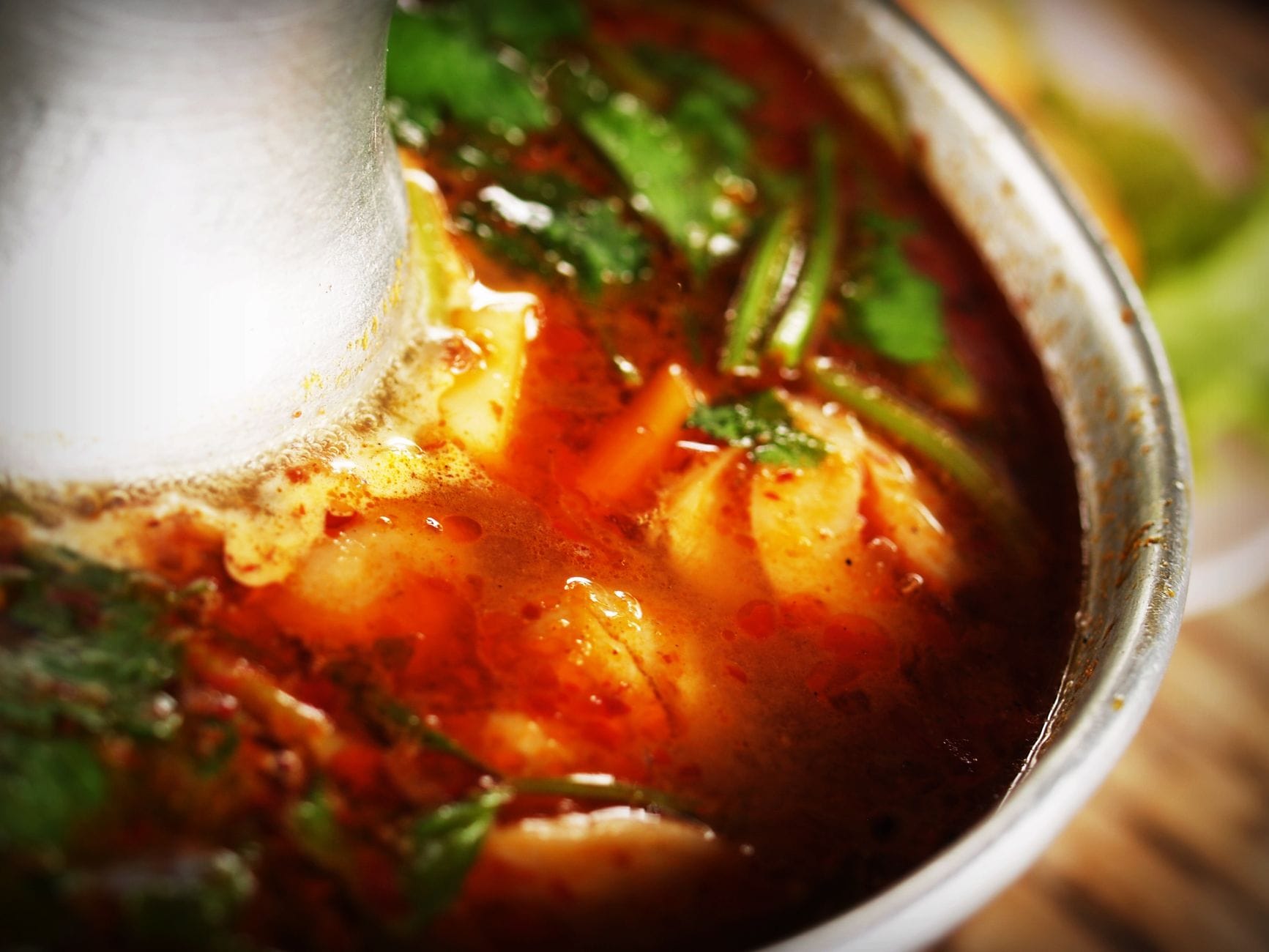 Zbliżenie tajskiej zupy Tom Yum z ziołami w metalowej misce
